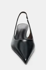 Zapato destalonado de piel negro, con punta fina y tacón kitten bajo y curvo. Posee una tira trasera con pieza elástica para ajuste en el talón.