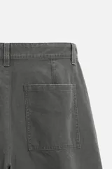 Pantalón gris oscuro de corte amplio, con bolsillos frontales y traseros de parche. Incluye un bolsillo lateral con cierre de cremallera.