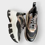 Zapatillas deportivas color beige con cordones a rayas en blanco y negro, suela de goma con plataforma y diseño chunky.