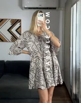 Vestido corto color verde oliva con estampado de hojas en blanco y negro, escote con lazo ajustable y mangas 3/4 acampanadas.