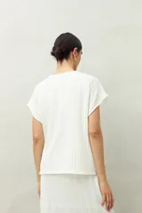 Top blanco de tejido texturizado con cuello redondo y mangas cortas tipo murciélago.