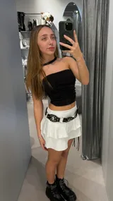 Minifalda blanca de tiro bajo con volados y cinturón negro con apliques metálicos.