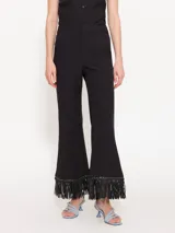 Pantalón negro de twill con corte acampanado y largo hasta el tobillo. El ruedo está terminado con flecos de cuerina al tono.