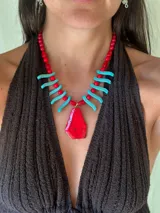 Collar de cuentas con dije central grande de piedra roja irregular, flanqueado por bastones turquesa y cuentas rojas redondas. La cadena es de eslabones finos con cierre regulable.