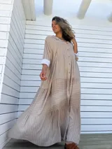 Vestido camisero largo color beige con rayas verticales blancas, cuello camisero, abotonadura frontal completa, mangas largas con puños abotonados y falda con volantes.