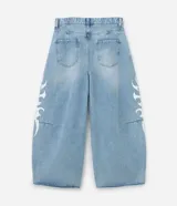 Pantalón de jeans celeste de corte amplio, con cintura con trabillas, cierre tradicional y bolsillos. Presenta estampa lateral estilo maorí en color blanco.