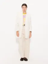 Saco color crema confeccionado en algodón, con bolsillos ojal, hombreras y aplique Groovy en el cuello.