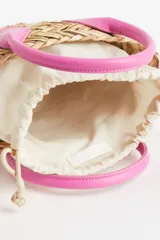 Cartera bandolera de paja color beige, con forro de tela color crema con cierre de cordón ajustable. Tiene dos asas cortas y correa larga ajustable de color rosa.