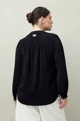 Camisa color marrón claro con cuello mao, mangas 3/4 abullonadas y cierre frontal con botones. Presenta pequeños pliegues en los hombros y detalle calado sutil.