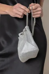 Cartera plateada recubierta con strass, con cierre de imán y cordón metálico para llevarla.
