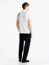 Chomba Tommy Hilfiger blanca con finas rayas horizontales celestes, corte regular, cuello clásico, tapeta de dos botones y logo bordado en el pecho.