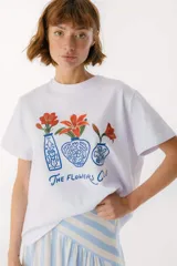 Remera blanca de algodón con estampado de tres jarrones con flores rojas y la frase "The Flowers Club" en azul.