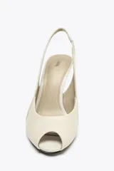 Zapato de tacón color crema, con puntera abierta y tira trasera ajustable.