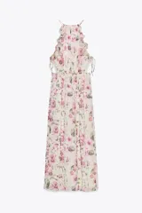 Vestido largo con estampado floral, cuello redondo y tirantes finos. Presenta elástico en la cintura con aberturas y lazadas laterales, volantes en el mismo tejido, forro interior a contraste y abertura frontal en el bajo. Cierre en la espalda con botón.