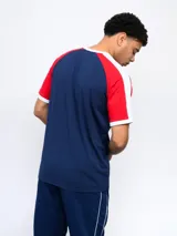 Remera de algodón azul con mangas ranglan azul marino y detalles en blanco en cuello y puños. Incluye logo de Umbro y escudo del Club Nacional de Football en el frente.