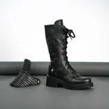 Borcego de cuero vacuno color negro, con suela de goma artesanal, caña alta con aplique capitoneado desmontable y horma de punta redonda.