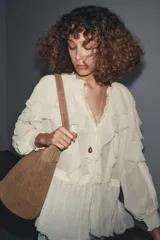 Blusa color crudo confeccionada en viscosa, con cuello redondo, escote en pico, mangas largas con puños elásticos, volantes frontales y detalles de encaje.