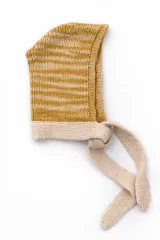 Capucha tejida a mano en lana merino con diseño de rayas horizontales en color mostaza y beige. Presenta una forma envolvente con lazos largos para anudar bajo el cuello, funcionando como un accesorio independiente de abrigo.