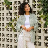 Llavero tipo cinta para colgar al cuello, color blanco crudo, con mosquetón metálico y detalle de parche de cuero claro con logo grabado.