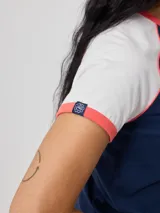 Remera azul marino de algodón con mangas cortas raglán blancas con ribete naranja y estampado ovalado con el logo de Rusty en el pecho.