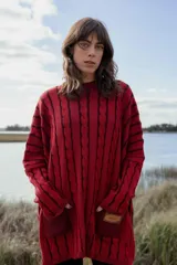 Vestido sweater rojo con diseño de trenzas verticales y rayas horizontales en negro. Tiene cuello redondo, mangas largas y bolsillos laterales.