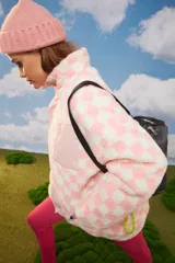 Abrigo oversized de poliéster simil corderito, con diseño a cuadros rosas y blancos. Tiene cuello alto, cierre frontal y bolsillo con cierre en el pecho.