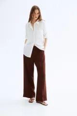 Pantalón ancho color marrón chocolate, de tiro alto con elástico en la parte posterior de la cintura y cierre oculto con corchete en un lado. Presenta bolsillos laterales discretos y piernas amplias con pliegues adelante y atrás.