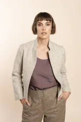 Chaqueta de sastrería color crudo con textura tweed, corte entallado, cuello mao y mangas largas.