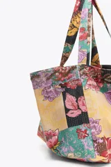 Maxi bolso de mano tipo tote bag con estampado floral multicolor sobre fondo amarillo.