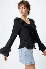 Blusa negra con escote en V y volados en el cuello y mangas largas acampanadas. Se ajusta con lazos finos al frente.