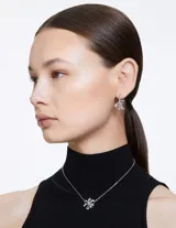 Conjunto de collar y aros Swarovski, modelo Volta, con baño de rodio y cristales transparentes engastados en forma de lazo.