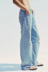 Pantalón de jean celeste claro, corte baggy, tiro medio, largo hasta el tobillo y con roturas grandes en ambas piernas.
