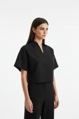 Remera negra de algodón, manga corta, corte ancho y holgado, estilo cropped y cuello polo.