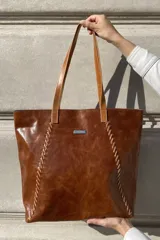 Bolso grande tipo tote de cuero color marrón con costuras decorativas en los laterales, forro interior con bolsillo para celular y bolsillo con cierre. Incluye bolsillo trasero con cierre y correas largas para colgar del hombro.