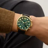 Reloj Guess Walker con caja dorada, esfera verde con tres subesferas y correa de cuero negro con textura.