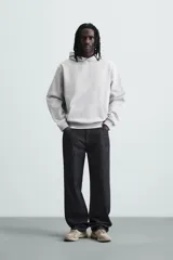 Sudadera con capucha color crudo, de corte relajado, confeccionada en tejido de algodón con interior rizado. Cuenta con cuello con capucha, manga larga, bolsillo frontal tipo canguro y acabados en rib.