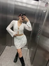 Conjunto de encaje blanco, compuesto por una chaqueta con lazos y una minifalda.