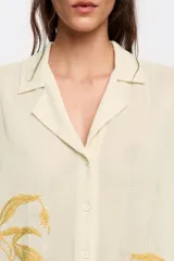 Camisa color crema con bordado de hojas color mostaza, de corte recto, manga corta y cuello camisero.