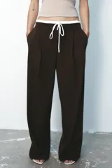 Pantalón ancho gris con textura de espiga, tiro alto, doble cintura elástica ajustable con cordón, pinzas frontales, bolsillos delanteros y falso bolsillo de vivo en la espalda.