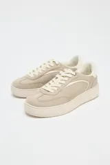 Zapatillas deportivas color beige, con suela alta de 3 cm y cierre con cordones.