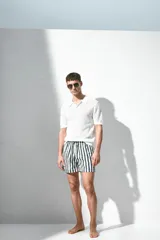 Short de baño blanco con rayas verticales verdes, cintura elástica con cordón ajustable, bolsillos laterales y bolsillo trasero con cierre autoadherente.
