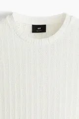 Remera blanca de punto calado con textura tipo crochet, corte estándar, cuello redondo y mangas cortas.