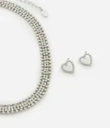 Conjunto de collar corto y aros tipo botón con forma de corazón, ambos plateados y con incrustaciones de estrás. Los aros tienen forma de corazón delineado con pequeñas esferas.