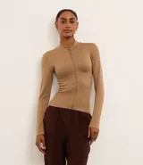 Campera deportiva color beige, de corte ajustado, confeccionada en tejido de poliamida seamless con textura acanalada y cuello alto. Posee cierre delantero por cremallera y mangas largas.