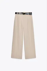 Pantalón ancho color beige, de tiro alto con pinzas delanteras, cinturón negro con hebilla dorada, bolsillos frontales y falsos bolsillos de doble vivo en la espalda.