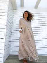 Vestido camisero largo color beige con rayas verticales blancas, cuello camisero, abotonadura frontal completa, mangas largas con puños abotonados y falda con volantes.