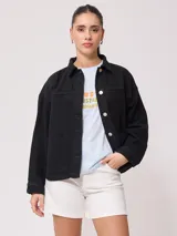 Sobrecamisa de mujer color negro, de corte recto, con cuello camisero, cierre frontal con botones a presión plateados, mangas largas con puños abotonados, dos bolsillos de parche en el pecho y dos bolsillos laterales. Confeccionada en algodón.