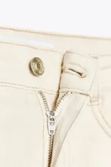 Pantalón de jean color crudo, de tiro alto, corte recto y largo tobillero. Tiene cinco bolsillos, cierre frontal con cremallera y botón metálico.