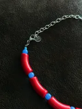 Gargantilla con cuentas de tubo acrílicas rojas y cristales checos azules. Se cierra con cadena de acero quirúrgico y ganchito para regular el largo.