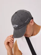 Gorra de gabardina color crudo con visera curva y logo de la marca bordado en negro en el frente.
